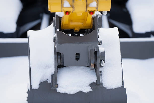 Close up of excavator bucket quick coupler and linkage covered with fresh snow
